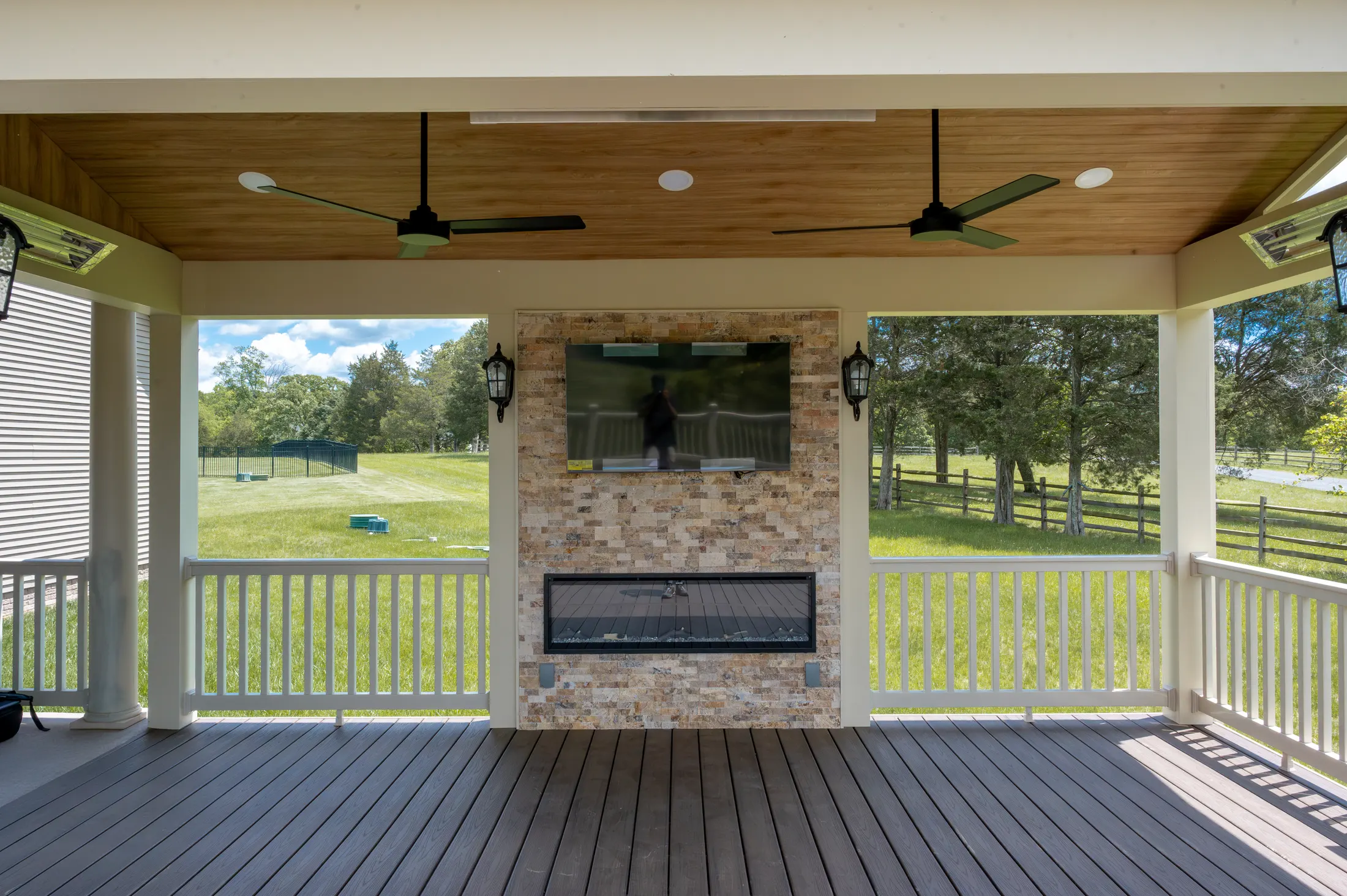 Covered deck with a wood ceiling, fans and a stone fireplace and TV wall